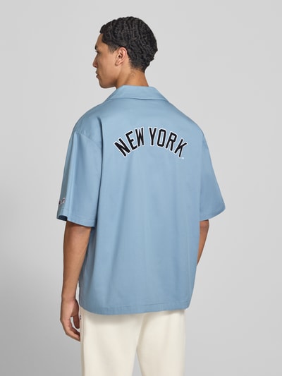 Männermodel trägt Relaxed Fit Freizeithemd aus Baumwoll-Mix von Champion in Hellblau mit Statement-Stitching, Ganzkörperansicht Rückansicht. Rückenlänge 74 cm, Schulterbreite 41 cm, Ärmellänge 36 cm, Reverskragen, Kurzarm.