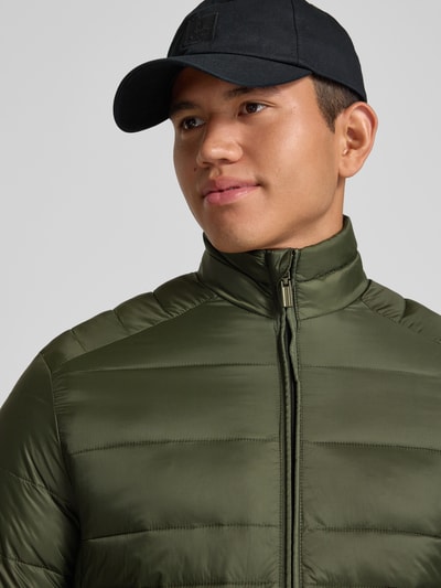 Męski model nosi Regular Fit kurtkę z efektem pikowania Model 'Kingsley' od JACK & JONES w kolorze oliwkowym, zamek błyskawiczny, wpuszczane kieszenie, stójka, tekstura matowa, Szerokość w rozmiarze M: 51 cm, Szerokość ramion w rozmiarze M: 48 cm, Długość tyłu w rozmiarze M: 72 cm, Długość rękawów w rozmiarze M: 68 cm, zbliżenie na górną część ciała.