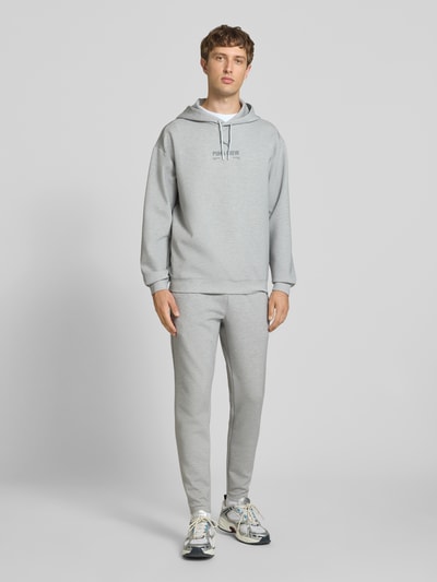 Männermodel trägt Hoodie mit Logo von PUMA PERFORMANCE in grau, Material-Mix mit Lyocell-Anteil, Relaxed Fit, Ganzkörperansicht von vorne.