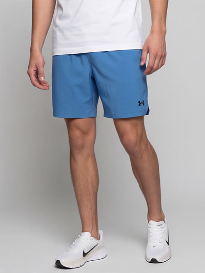 Männermodel trägt blaue Regular Fit Sportshorts mit Logo-Print von Under Armour, glatte Oberfläche, weiße Sneaker, Nahaufnahme Oberschenkel, Herren Sportshorts von Under Armour.