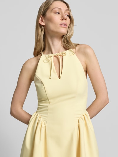 Frauenmodel trägt Cocktailkleid mit Schlüsselloch-Ausschnitt von Little Mistress in zartem Gelb, Material-Mix mit Rayon-Anteil, A-Linie, Minikleid, Schnürung und rückseitigem Reißverschluss, Rückenlänge 83 cm, Brustweite 40 cm, Nahaufnahme Oberkörper.