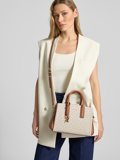 Frauenmodel trägt Handtasche mit Label-Applikation Modell 'LAILA' von MICHAEL Michael Kors in Beige, Ganzkörperansicht von vorne, Hauptfach mit Reißverschluss, Tragehenkel und Schulterriemen, Maße: Breite 29 cm, Länge 19 cm, Tiefe 10 cm, Schulterriemen 132 cm.