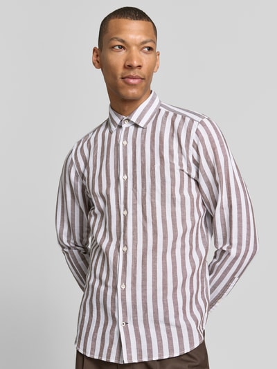 Männermodel trägt Slim Fit Business-Hemd mit Kentkragen Modell 'Pit' von JOOP! Collection im Baumwoll-Leinen-Mix mit braun-weißen Längsstreifen, Knopfleiste und Sportmanschetten, Ganzkörperansicht von vorne.