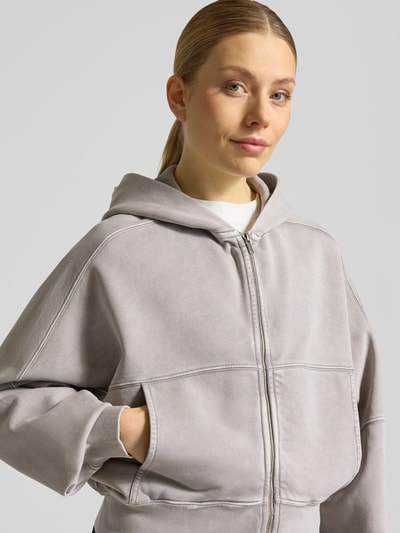 Frauenmodel trägt Sweatjacke mit Zweiwege-Reißverschluss Modell 'RANERA' von Drykorn in Grau, Reine Baumwolle, Relaxed-Fit, Kapuze. Nahaufnahme Oberkörper.
