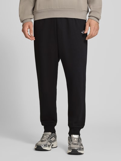 Mężczyzna nosi Relaxed Fit Sweatpants aus Baumwoll-Mix Modell 'EVOLUTION' von The North Face, czarny kolor, wpuszczane kieszenie, elastyczny pas z tunel, styl casualowy, mieszanka bawełny, długość wewnętrzna nogawki w rozmiarze M: 75 cm, Ganzkörperansicht z przodu.