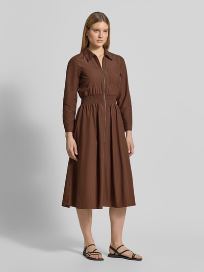 Frauenmodel trägt Hemdblusenkleid mit Reißverschluss Modell 'NETTI' von Soyaconcept in Braun, A-Linie, Midikleid, Material-Mix mit Baumwoll-Anteil, elastisches Taillenband, glatte Textur, Ganzkörperansicht von vorne. Rückenlänge bei Größe S: 121 cm, Brustweite: 42 cm, Ärmellänge: 60 cm.
