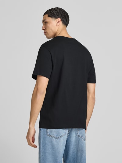 Männermodel trägt T-Shirt mit Label-Stitching von Calvin Klein Jeans in Schwarz aus Reine Baumwolle, Slim-Fit, Rückenansicht, Rückenlänge 70 cm in Größe M, Rundhalsausschnitt, kombiniert mit Jeans.