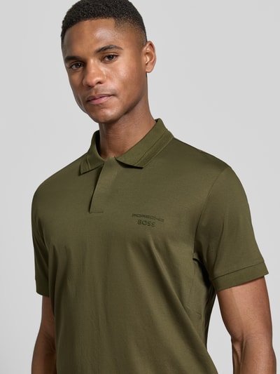Männermodel trägt Regular Fit Poloshirt aus reiner Baumwolle Modell 'PS Spirit 70 Plk' von BOSS Green X PORSCHE in Olive, Nahaufnahme Oberkörper.