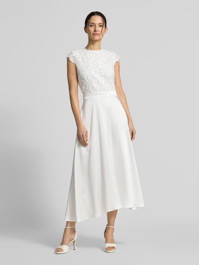 Frauenmodel trägt Brautkleid in Midilänge Modell 'Lilia' von GUIDO MARIA KRETSCHMER WOMAN, Spitze oben, Satin unten, tailliert, Ganzkörperansicht von vorne.