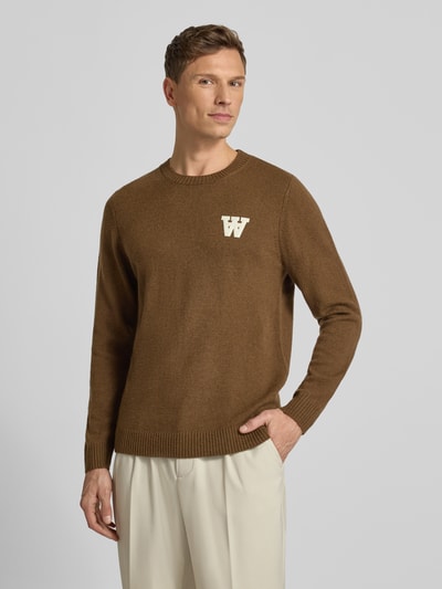 Männermodel trägt Strickpullover aus Lammwolle Modell 'Tay' von Wood Wood, Reine Lammwolle, Regular-Fit, Label-Stitching, Rundhalsausschnitt, Vorderansicht Oberkörper.