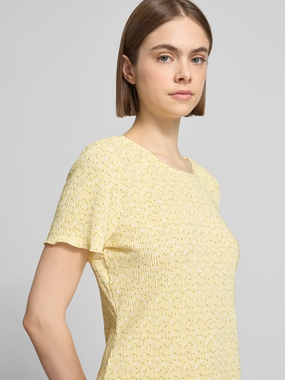 Frauenmodel trägt Slim Fit T-Shirt mit Allover-Muster Modell 'FLORA' von Pieces in Gelb mit Plissee, florales Muster, Nahaufnahme Oberkörper.