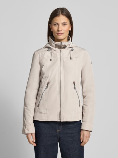 Modelka kobieca nosi Jacke mit Kapuze und Reißverschlusstaschen od Gil Bret w kroju regular fit, beżowa, z kapturem z troczkiem, stójką, zamkiem i kieszeniami na zamek, długość tyłu w rozmiarze 36: 59 cm, szerokość ramion: 40 cm, szerokość w klatce: 51 cm, długość rękawa: 63 cm, gładka faktura, widok całej sylwetki z przodu