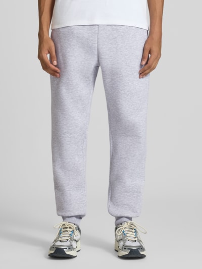 Mężczyzna nosi Slim Fit Sweatpants mit Tunnelzug von REVIEW, jasnoszary kolor, wpuszczane kieszenie, kieszeń z tyłu, krój slim fit, elastyczny pas z tunelem, długość wewnętrzna nogawki w rozmiarze M: 80 cm, Ganzkörperansicht von vorne.