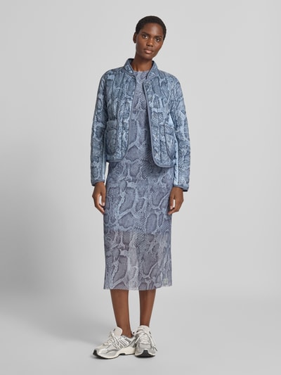 Frauenmodel trägt Regular Fit Jacke in Stepp-Optik mit Stehkragen von Marc Cain im blauen Allover-Schlangen-Print, aufgesetzte Taschen, durchgängige Knopfleiste, kombiniert mit passendem Kleid und Sneaker, strukturierte Oberfläche, Ganzkörperansicht von vorne. Rückenlänge bei Größe 36: 56 cm, Schulterbreite: 43 cm, Brustweite: 50 cm, Ärmellänge: 60 cm.