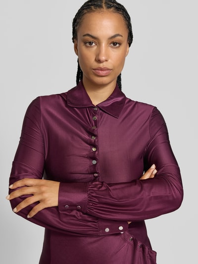 Frauenmodel trägt Knielanges Kleid aus Viskose-Mix von Rabanne in dunklem Beerenton, taillierte Passform, Umlegekragen, Knopfleiste mit Raffungen, langärmelig, seidige Textur, Nahaufnahme Oberkörper.
