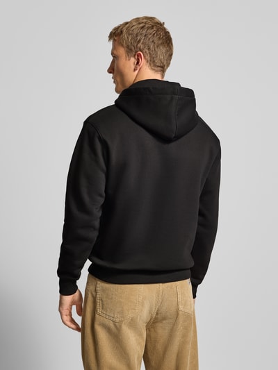 Männermodel trägt Hoodie mit Logo und Känguru-Tasche von Alpha Industries aus schwarzem Baumwoll-Mix, Regular-Fit, Rückenlänge 67 cm, Ärmellänge 64 cm, Ganzkörperansicht Rückansicht.
