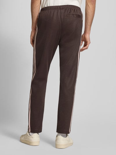 Männermodel trägt 'Sweatpants mit elastischem Bund' von adidas Originals in Braun mit rosa Streifen, lockerer fit, Gesäßtasche, Rückansicht Ganzkörperansicht.