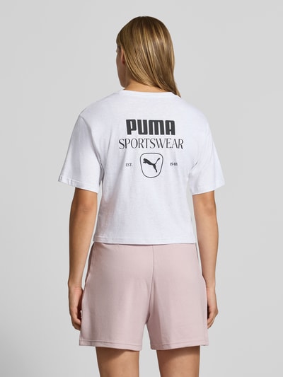 Frauenmodel trägt Relaxed Fit T-Shirt aus reiner Baumwolle von PUMA in Weiß mit schwarzem Logo, dazu hellrosa Shorts, Ganzkörperansicht Rückansicht, Damen T-Shirt von PUMA.