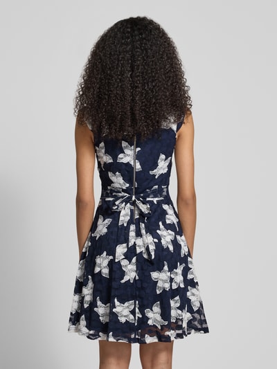 Männermodel trägt Minikleid im Allover-Look mit Rundhalsausschnitt von Apricot, granatowy materiał z białym wzorem, A-linia, długość tyłu w rozm. S: 88 cm, szerokość w rozmiarze S: 40 cm, materiał elastyczny, widok całej sylwetki z tyłu