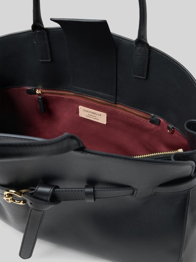 Produktfoto, Torba shopper z uchwytem, model 'SABINE' od Coccinelle, główna przegroda z zapięciem na magnes, przegródka wewnętrzna na zamek, detal z logo, wymiary: szerokie 40 cm, długość 32 cm, głębokość 16 cm, pasek na ramię 37 cm, kolor czarny z bordową podszewką, tekstura gładka
