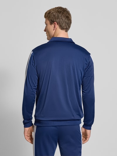 Männermodel trägt Trainingsanzug mit elastischen Abschlüssen von adidas Sportswear w kolorze granatowym, proste formy, tkanina gładka, ganzkörperansicht rückansicht. Szerokość w rozmiarze M: 36 cm, długość tyłu: 71 cm, szerokość ramion: 46 cm, długość rękawów: 63 cm, długość wewnętrzna nogawki: 75 cm.
