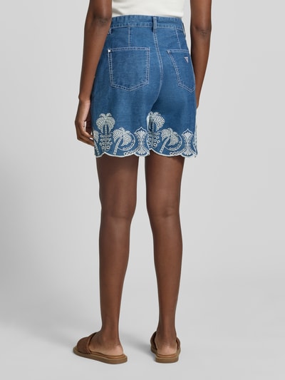 Frauenmodel trägt Shorts mit Lochstickerei Modell 'PILAR' von Guess aus reiner Baumwolle im Wide-Fit, blaue Farbe, Ganzkörperansicht Rückansicht.