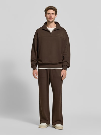 Męski model nosi Relaxed Fit Sweatshirt aus Baumwoll-Modal-Mix von Tommy Hilfiger w kolorze brązowym, szerokie nogawki, jednolita faktura, bluza i spodnie, widok całej sylwetki z przodu.