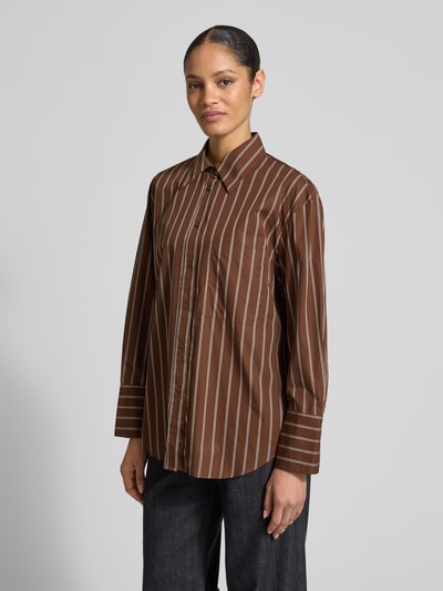 Frauenmodel trägt Relaxed Fit Hemdbluse mit Brusttasche Modell 'LLAMA' von Mango in Braun mit weißen Streifen aus reiner Baumwolle, Hemdblusenkragen und Knopfleiste, Ganzkörperansicht von vorne.