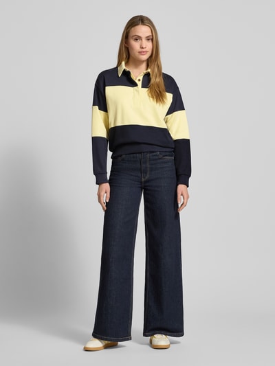 Modelka kobieca nosi Sweatshirt mit Polokragen und Label-Stitching od Gant z bawełny, kolor granatowy i żółty, relaxed fit, widok całej sylwetki z przodu.
