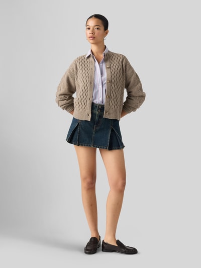 Frauenmodel trägt Ausgestellter Mini-Rock aus reiner Baumwolle von Levi's® in Dunkelblau, kombiniert mit heller Strickjacke und Hemd, Ganzkörperansicht von vorne. Damen Mini-Rock von Levi's®.