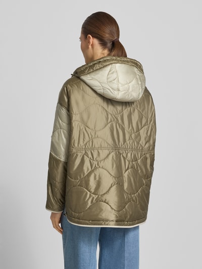 Frauenmodel trägt Steppjacke mit aufgesetzten Eingrifftaschen und Kapuze von Blonde No. 8 in glänzendem Khaki, strukturierte Oberfläche, Ganzkörperansicht Rückansicht. Stil: gerader Schnitt, Kapuze mit Kordelzug und Druckknöpfen, Knopfverschluss, verstellbarer Saum.
