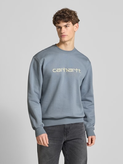 Männermodel trägt Sweatshirt mit Label-Stitching von Carhartt Work In Progress in blaugrauem Baumwoll-Mix, lockere Passform, Ganzkörperansicht von vorne.