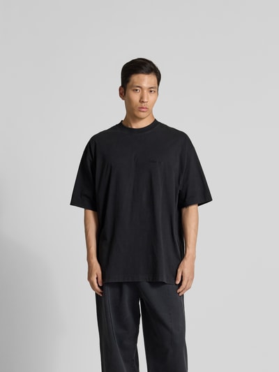 Männermodel trägt Oversized T-Shirt aus Baumwolle von VETEMENTS in Schwarz mit Rundhalsausschnitt, lockerer Schnitt, Ganzkörperansicht von vorne.