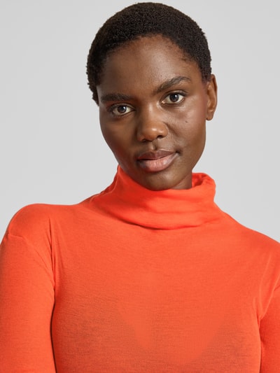 Frauenmodel trägt Slim Fit Rollkragenshirt aus reiner Baumwolle von American Vintage in leuchtendem Orange, fein gerippt, Ziernähte, Nahaufnahme Oberkörper.