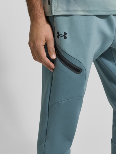Mężczyzna nosi Sweatpants mit Logo Modell 'Unstoppable' od Under Armour, kolor jasnoniebieski, bawełniany materiał, zbliżenie na biodro.
