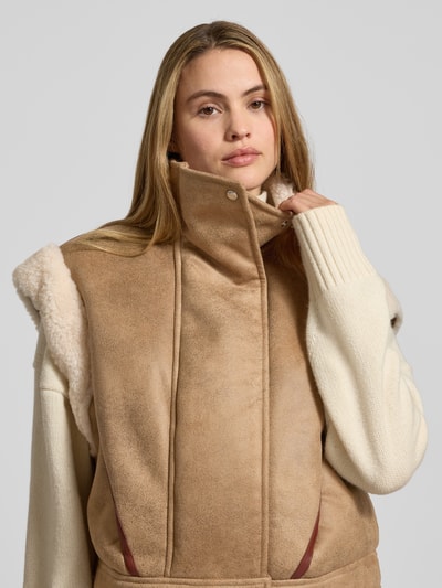 Kobiece model prezentuje Regular Fit Jacke in Lederoptik mit abnehmbaren Ärmeln Modell 'CHEERLEA' od BOSS Orange w beżowej, skórzanej fakturze z białymi, długimi rękawami i kołnierzem, zamek błyskawiczny, kieszenie boczne; zbliżenie na górną część ciała.