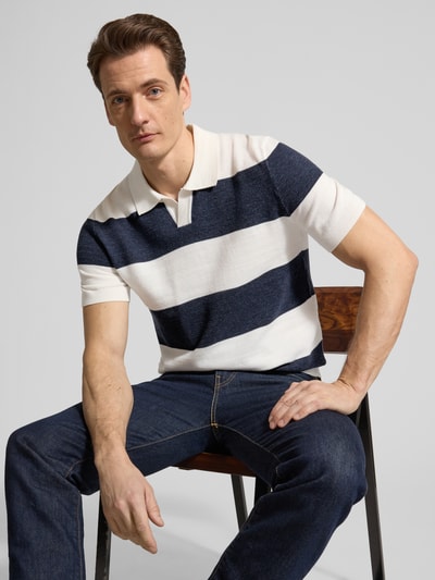 Männermodel trägt Slim Fit Poloshirt aus Baumwoll-Mix in Strick-Optik von OLYMP Level Five, marineblau-weiß gestreift, krój slim fit, Umlegekragen, kurzärmelig, elastische Abschlüsse, Ganzkörperansicht von vorne.