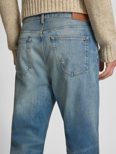 Männermodel trägt Tapered Fit Jeans aus reiner Baumwolle Modell 'SONNY' von Tommy Jeans in Denim Used-Look mit Label-Patch, Nahaufnahme Rückansicht.