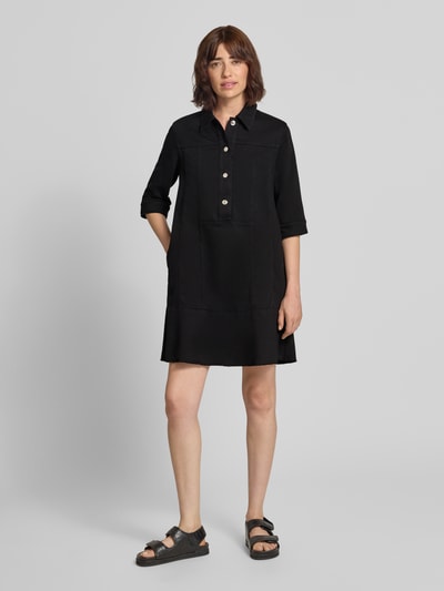 Frauenmodel trägt knielanges Hemdblusenkleid mit Knopfleiste und 1/2-Arm von Marc Cain in Schwarz, gerader Schnitt, Ganzkörperansicht von vorne.