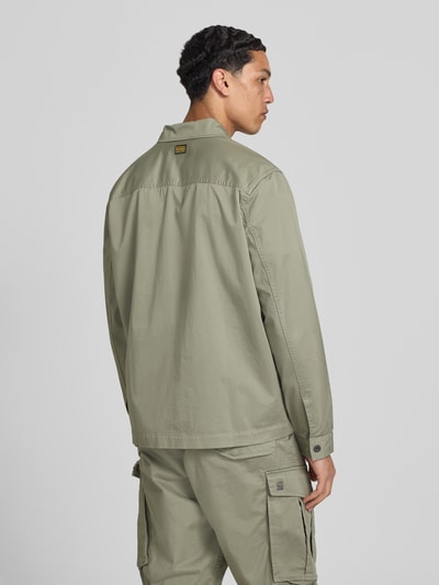Męski model nosi Hemdjacke mit Kentkragen und Brusttaschen od G-Star Raw w kolorze jasnej oliwki, krój regular fit, listwa guzikowa, kieszenie na piersi, długość tyłu w rozmiarze M: 45 cm, szerokość ramion w rozmiarze M: 61 cm, szerokość klatki piersiowej w rozmiarze M: 58 cm, długość rękawów w rozmiarze M: 67 cm, całkowity widok z tyłu.