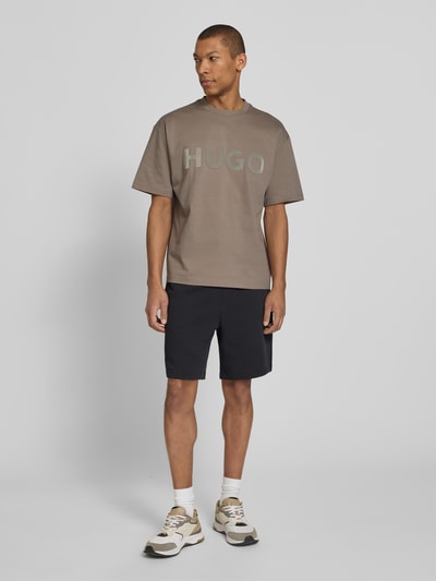 Männermodel trägt Relaxed Fit T-Shirt aus reiner Baumwolle Modell 'DINKEE' von HUGO, unifarben, 3D Label Print, Ganzkörperansicht von vorne.