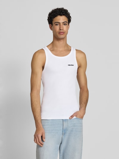 Męski model nosi Tanktop in Ripp-Optik mit Logo od REVIEW z bawełny, krój slim fit, efekt prążkowania, logo, okrągły dekolt, długość tyłu w rozmiarze M: 67 cm, jasne kolory, prosta tekstura, całkowite ujęcie z przodu.