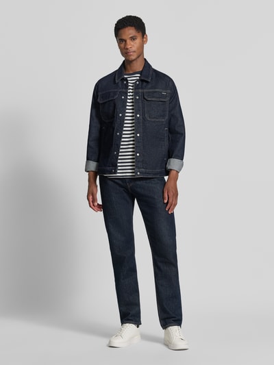 Męski model nosi Slim Fit Jeansjacke aus Baumwoll-Mix von Antony Morato, ciemnoniebieska mieszanka bawełny i elastanu, wykładany kołnierz, kieszenie na piersi i wpuszczane kieszenie, listwa z zatrzaskami na całej długości, długość tyłu w rozmiarze 50: 67 cm, szerokość ramion w rozmiarze 50: 42 cm, szerokość w rozmiarze 50: 55 cm, długość rękawów: 67 cm, cała sylwetka z przodu.
