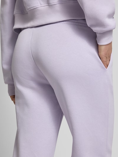 Kobiece modelka nosi Sweatpants mit elastischem Bund Modell 'Iconic' od Gina Tricot, bawełniany mix, krój relaxed fit, z elastycznym pasem i troczkiem, kolor jasnofioletowy, gładka tekstura, długość nogawki 80 cm w rozmiarze S, detailaufnahme tylnej części.