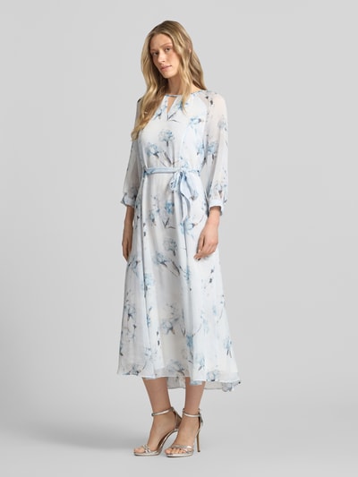 Frauenmodel trägt Midikleid mit Bindegürtel von More & More, blauer Blumenprint, Taillierter Schnitt, Rundhalsausschnitt mit Cut-Out, 3/4-Arm, Rückseitiger Schlüsselloch-Ausschnitt und Reißverschluss, Rückenlänge 128 cm bei Größe 36, Brustweite 42 cm, Ärmellänge 58 cm, Ganzkörperansicht von vorne.