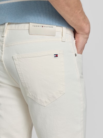 Männermodel trägt Straight Fit Jeans aus Baumwoll-Mix Modell 'DENTON' von Tommy Hilfiger, efekt: jednolity kolor, nity, wyhaftowane logo, naszywka z logo, denim, mieszanka bawełny, detal z 5 kieszeni, zapięcie na guzik i zamek błyskawiczny, widok z tyłu detalaufnahme.