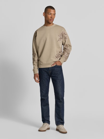 Männermodel trägt Regular Fit Sweatshirt Modell 'Kario' von Drykorn aus Reiner Baumwolle mit Florales Allover-Stitching, Rundhalsausschnitt, Elastische Abschlüsse, Beige und Braun, Rückenlänge 62 cm, Ärmellänge 65 cm, Ganzkörperansicht von vorne.