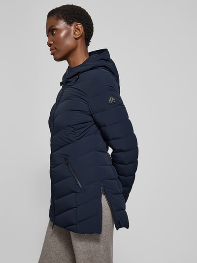 Frauenmodel trägt Daunenjacke mit Kapuze von Moose Knuckles in Dunkelblau, Material-Mix mit Stretch-Anteil, taillierter Schnitt, Ganzkörperansicht von vorne.
