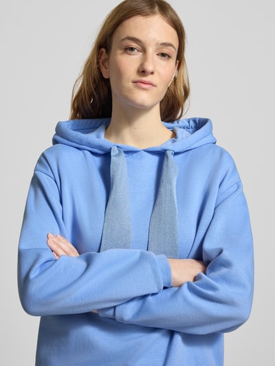 Modelka kobieca nosi Regular Fit Hoodie aus Baumwoll-Mix Modell 'CHILLI' od Pieces, niebieski, jednolity, materiał sweat, z kapturem, widok na górną część ciała z przodu.