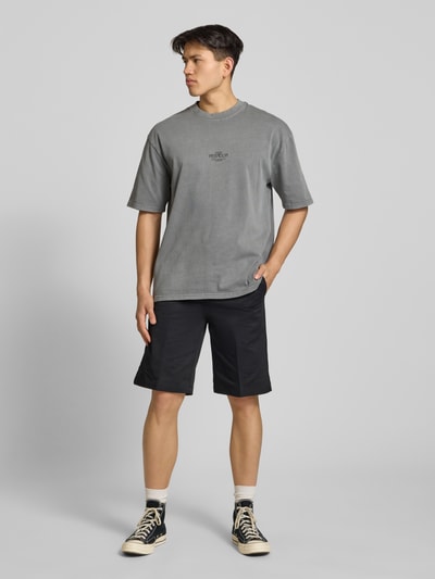 Mężczyzna model nosi Oversized T-Shirt mit 1/2-Arm Modell 'Trebic' von Pegador z czystej bawełny w szarym kolorze, nadruk z przodu, krój oversize, okrągły dekolt, detal z logo, długość pleców w rozmiarze M: 70 cm, Ganzkörperansicht von vorne.